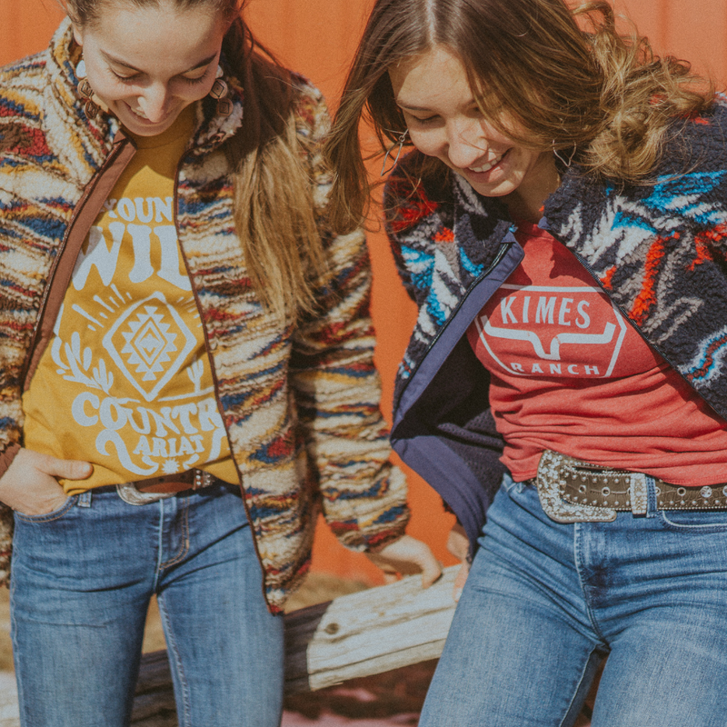 Two women wearing colorful jackets with visible branding against an orange background