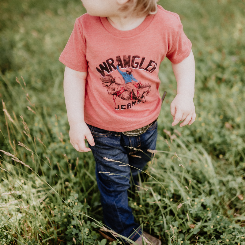 Child wearing a red Wrangler shirt standing in a grassy field