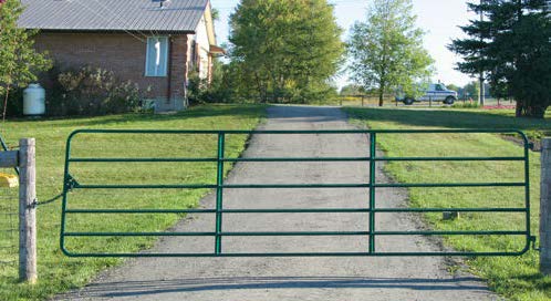 Open metal gate on a driveway leading to a house with trees in the background